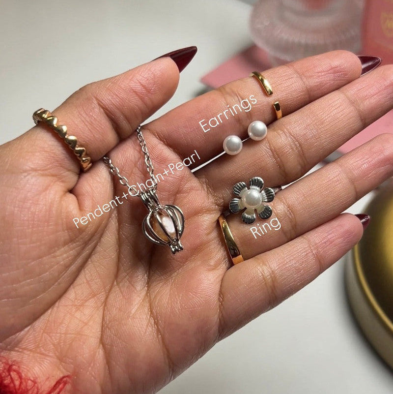 Hand holding jewelry including earrings, a pendant, and a ring on a light background.